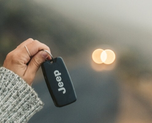 Person holding up jeep key toward blurry road - Jeep performance chips improve gas mileage